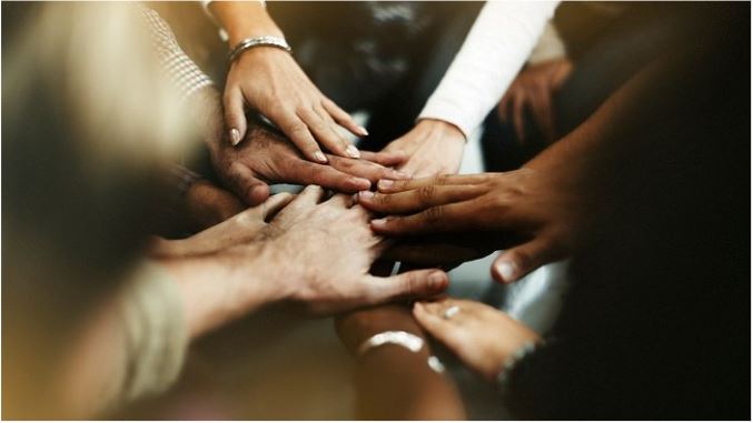 A diverse group of people laying their hands on top of each other.