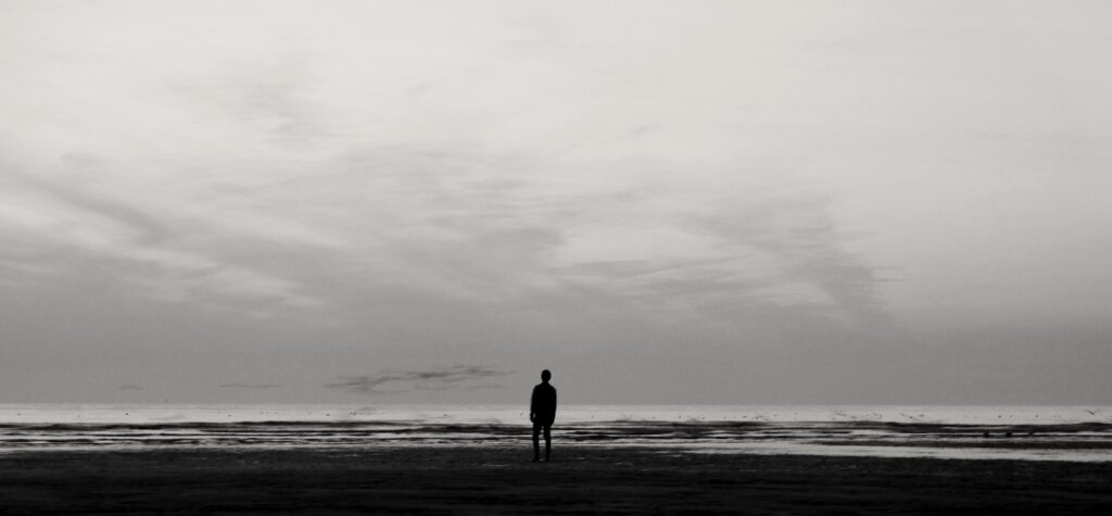 A man standing on the beach near the water's edge.