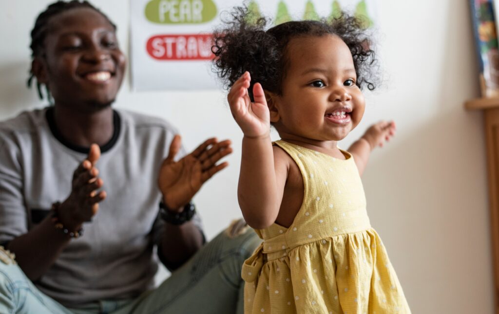 A young toddler learning to walk in front of a happy father. 