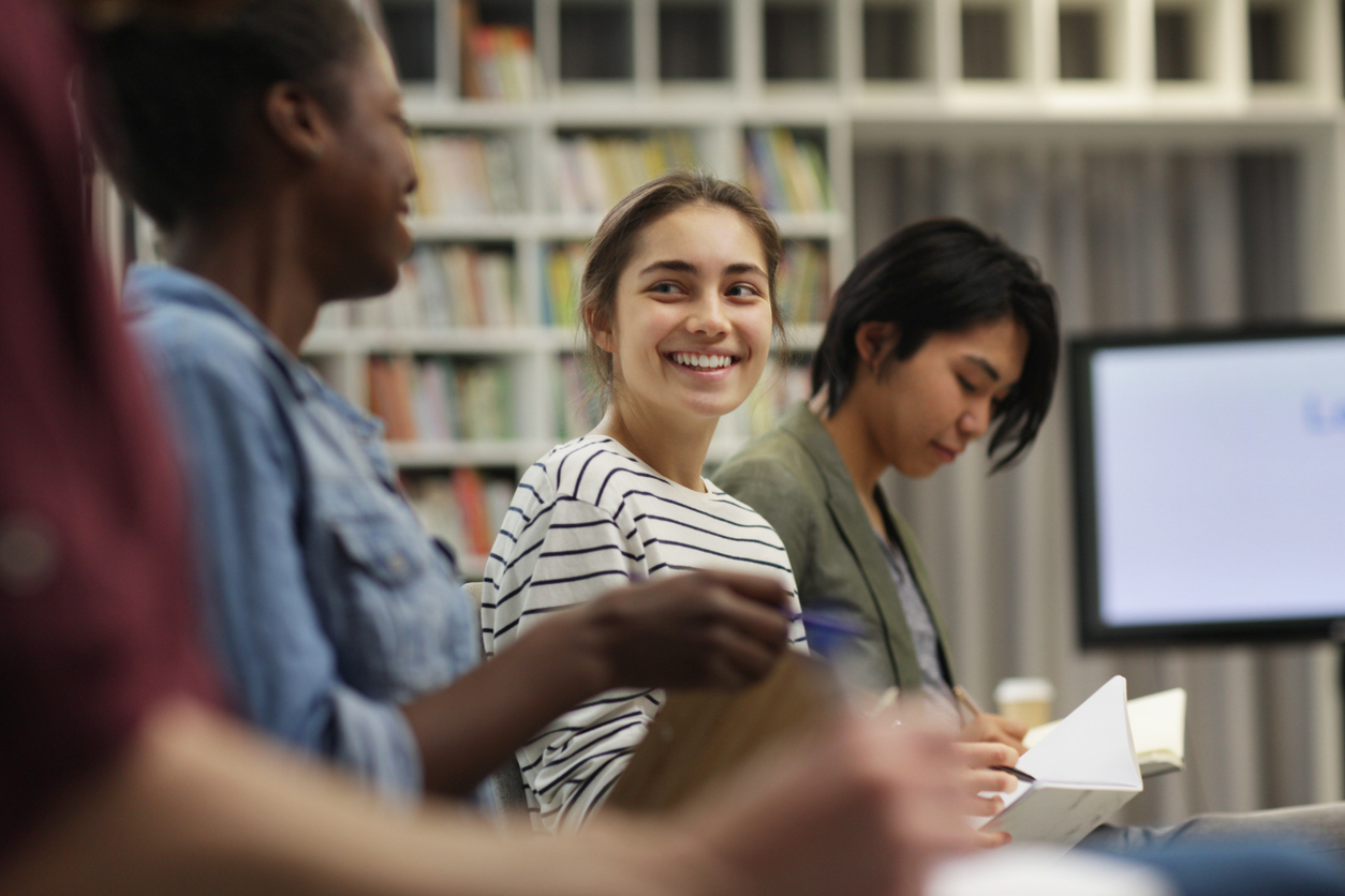 Young woman sitting and smiling while talking to her peers during a seminar