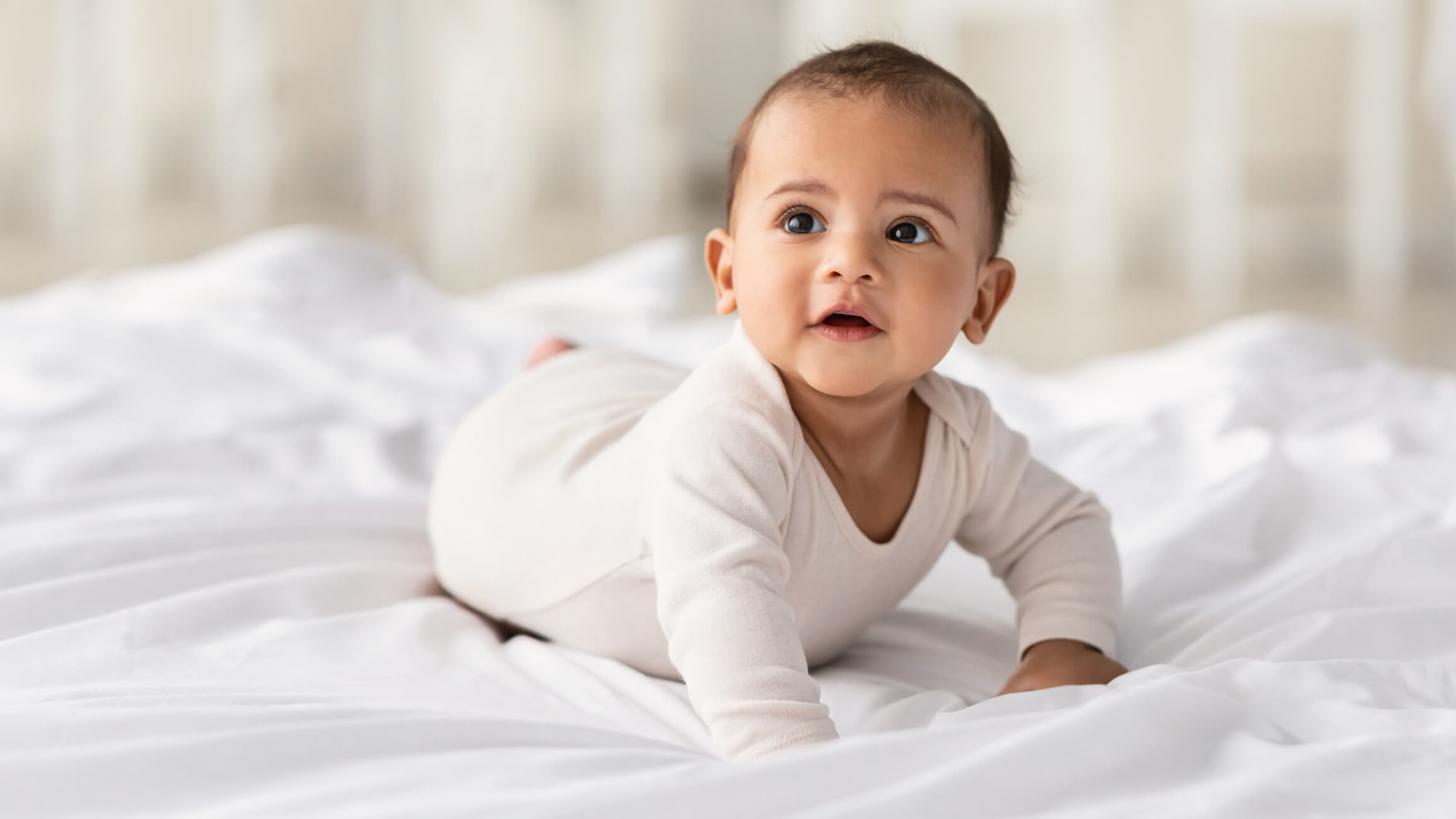 Portrait of cute little baby wearing bodysuit lying on white bedsheets