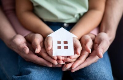 Man, woman and little child holding cutout paper house figure in hands.