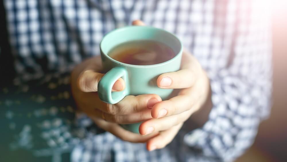 Hands around a green mug of steaming tea