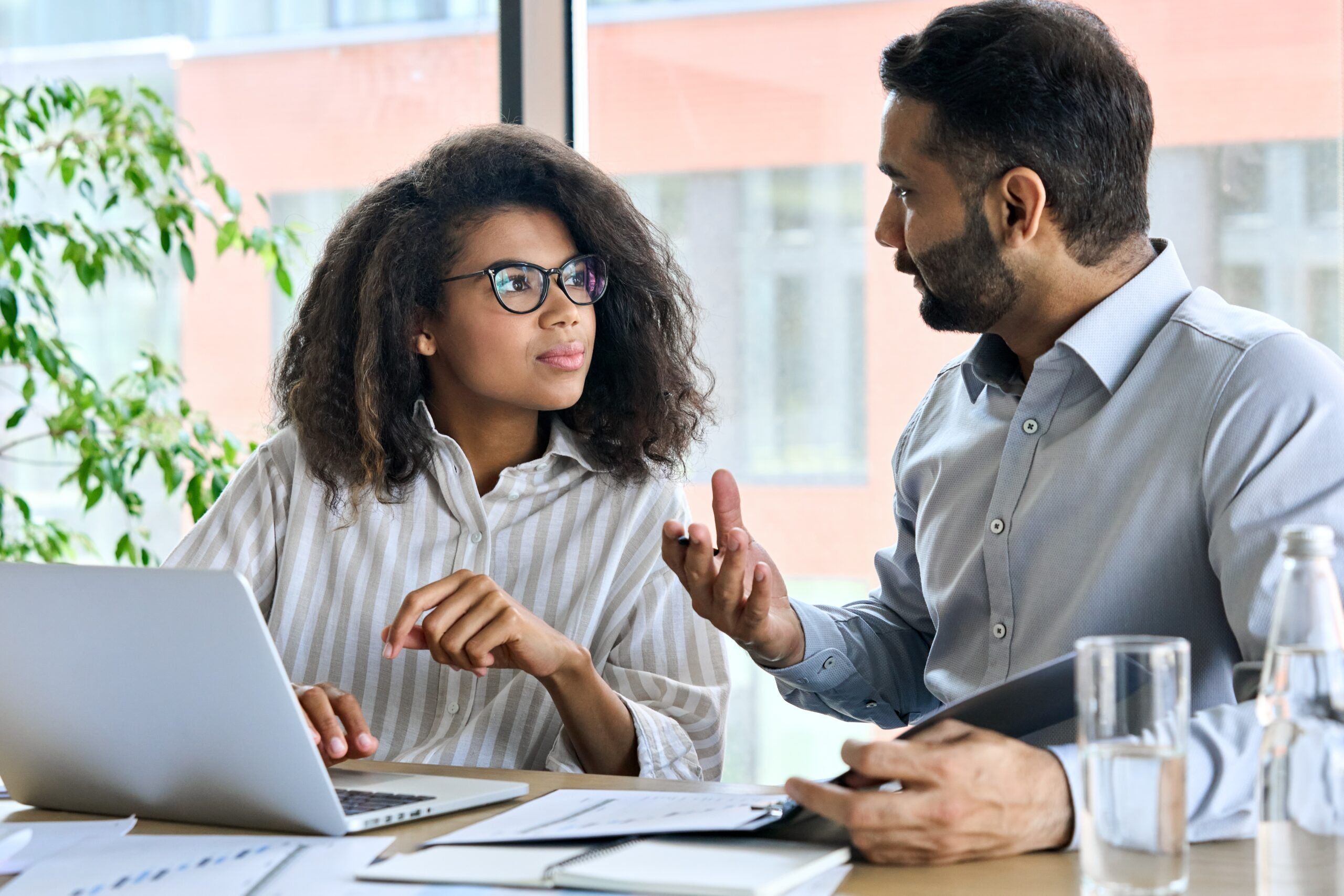 Two people in smart clothes having a conversation with nots and laptop on desk