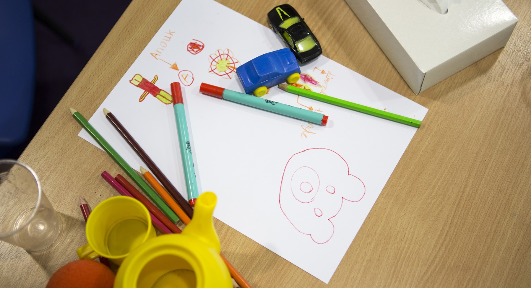 Coloured pencils, paper and toys on a table.
