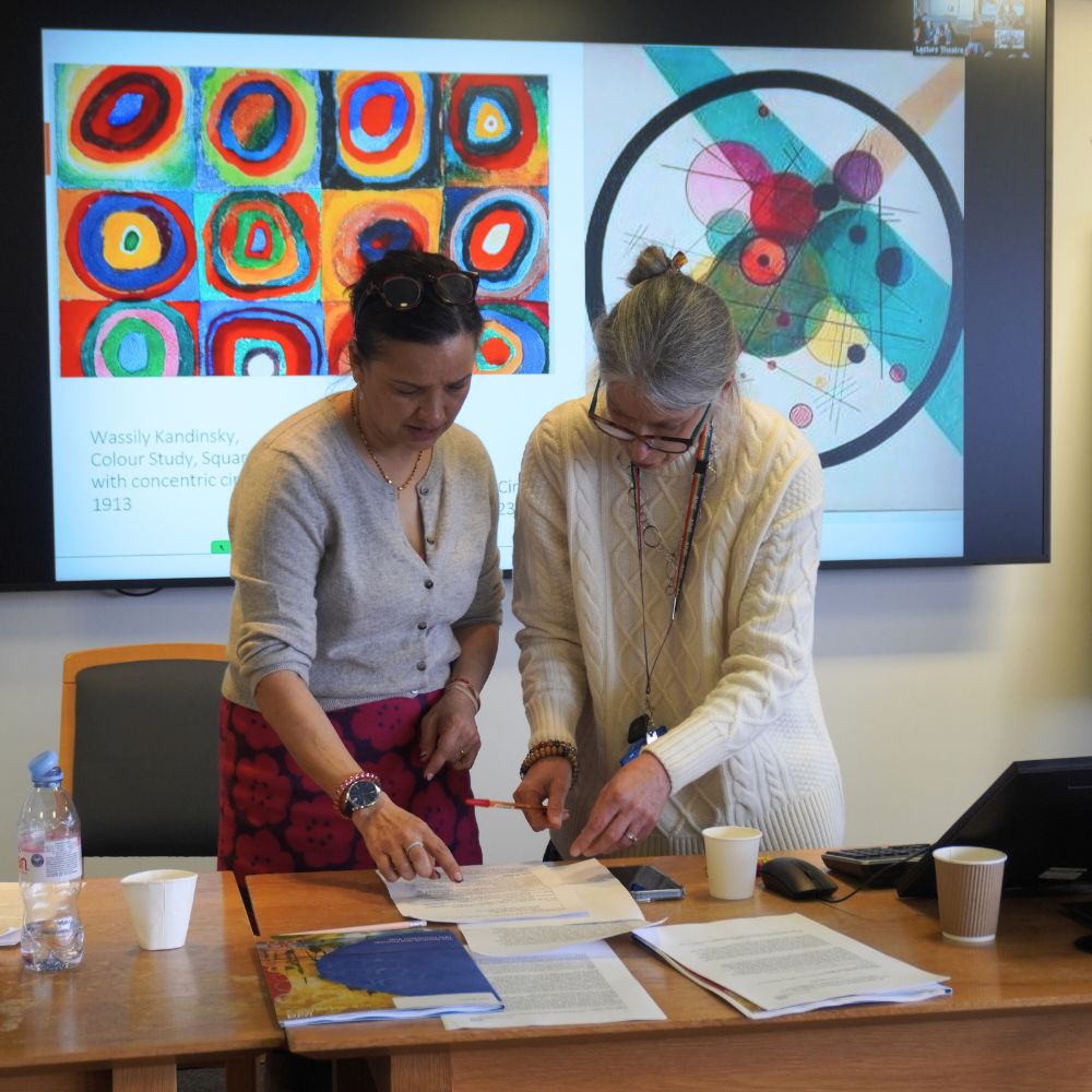 Two presenters looking over notes in front of a presentation screen.