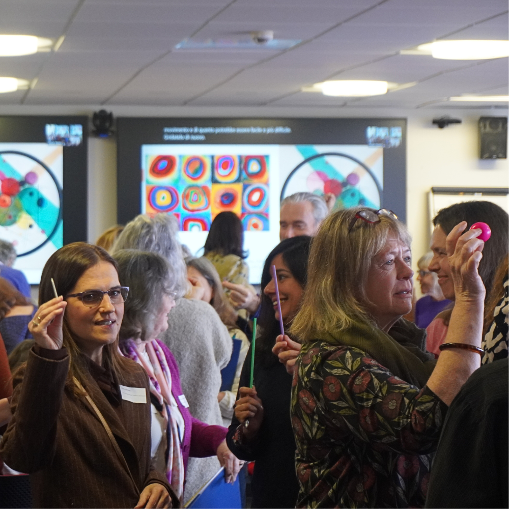 Interactive workshop at the 2024 Infant observation conference. Delegates are holding bright objects in the air including straws and a bouncy ball.