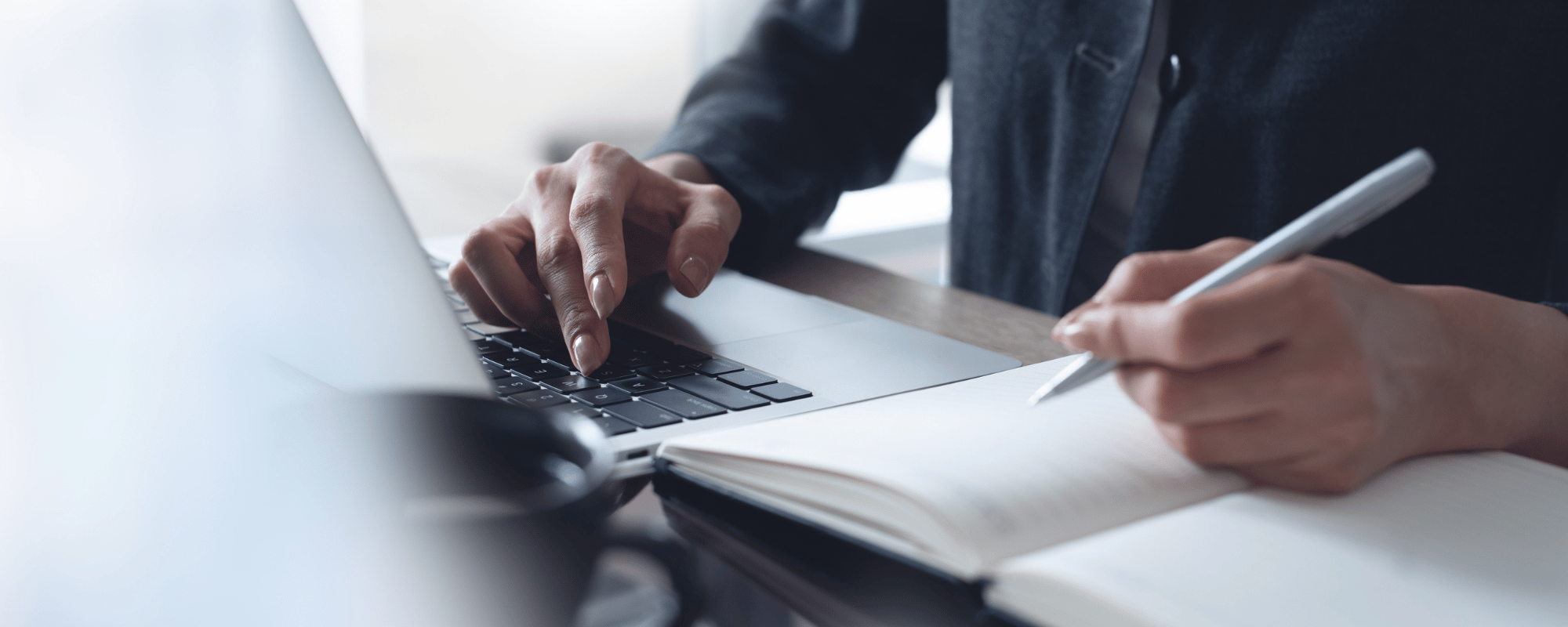 Close-up of a person's hands working with a keyboard and notebook.