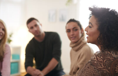 Women talking with peers who are sat in a semi-circle with their heads turned in and listening
