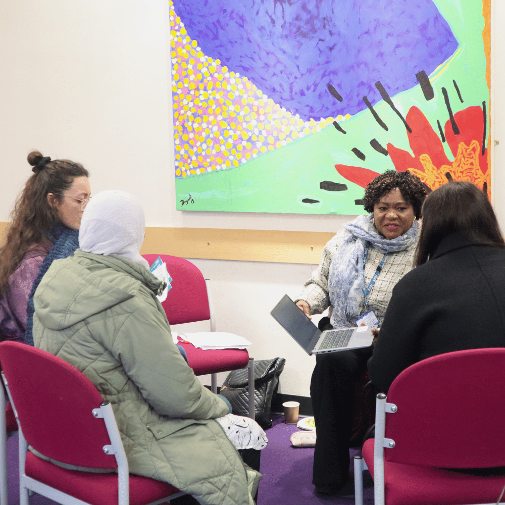 Small group circle sat in red chairs with a bright abstract painting in the background